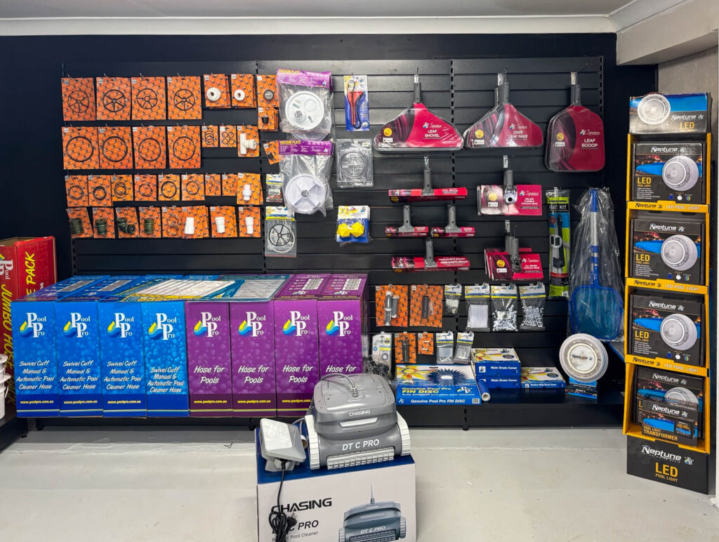 Pool equipment display wall at Pool Pro Parkes featuring a robotic pool cleaner, Neptune LED pool lights, and pool vacuum accessories.